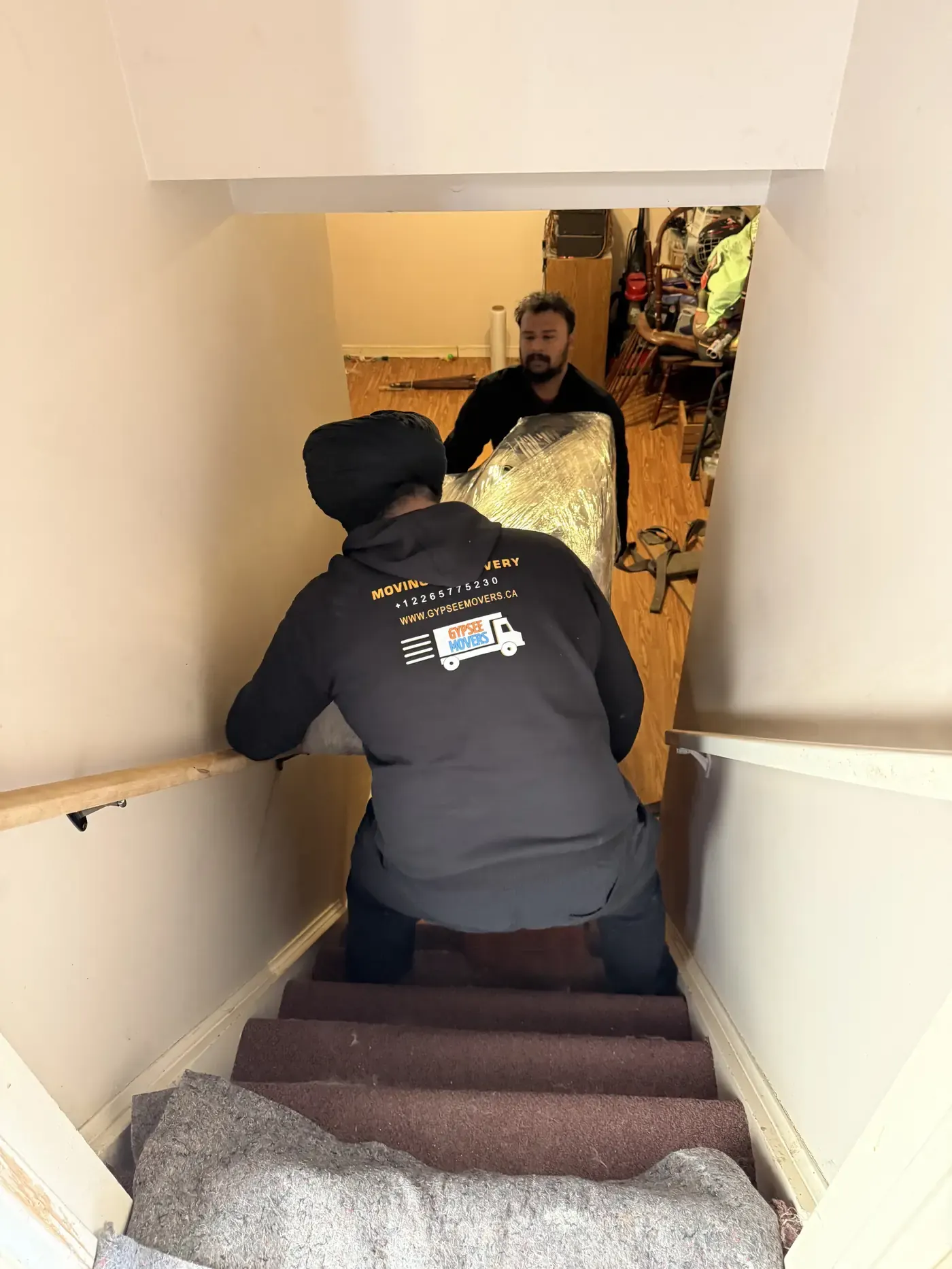 Commercial movers carrying a wrapped item down stairs during a business move