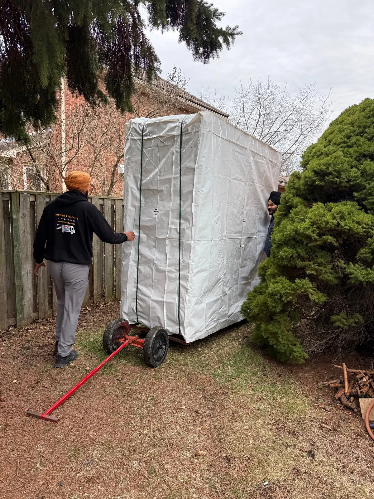 Movers bringing a wrapped hot tub through a backyard access path