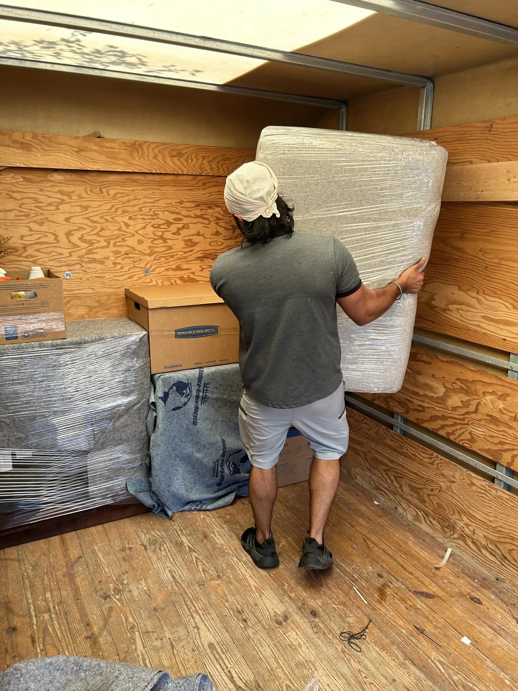 Mover placing wrapped mattress inside moving truck