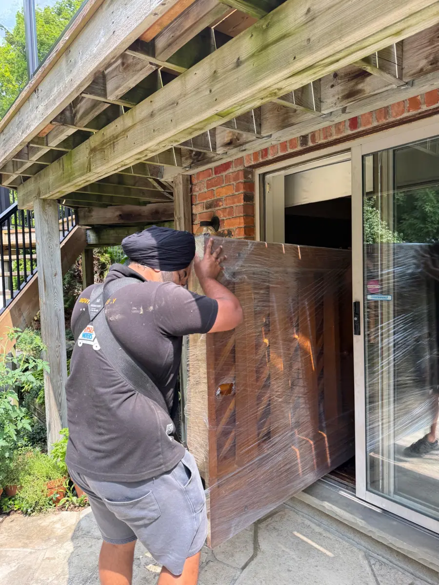 Professional movers carefully extracting a piano through an exterior doorway