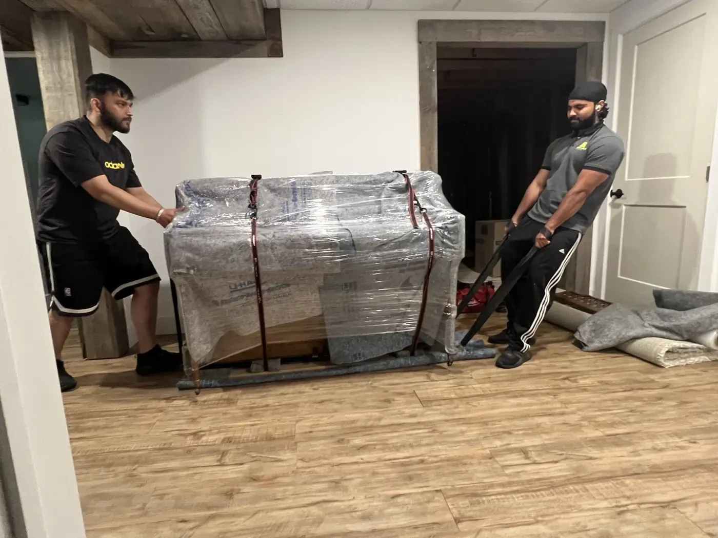 Piano movers using blankets to protect stairs and floors while moving a piano