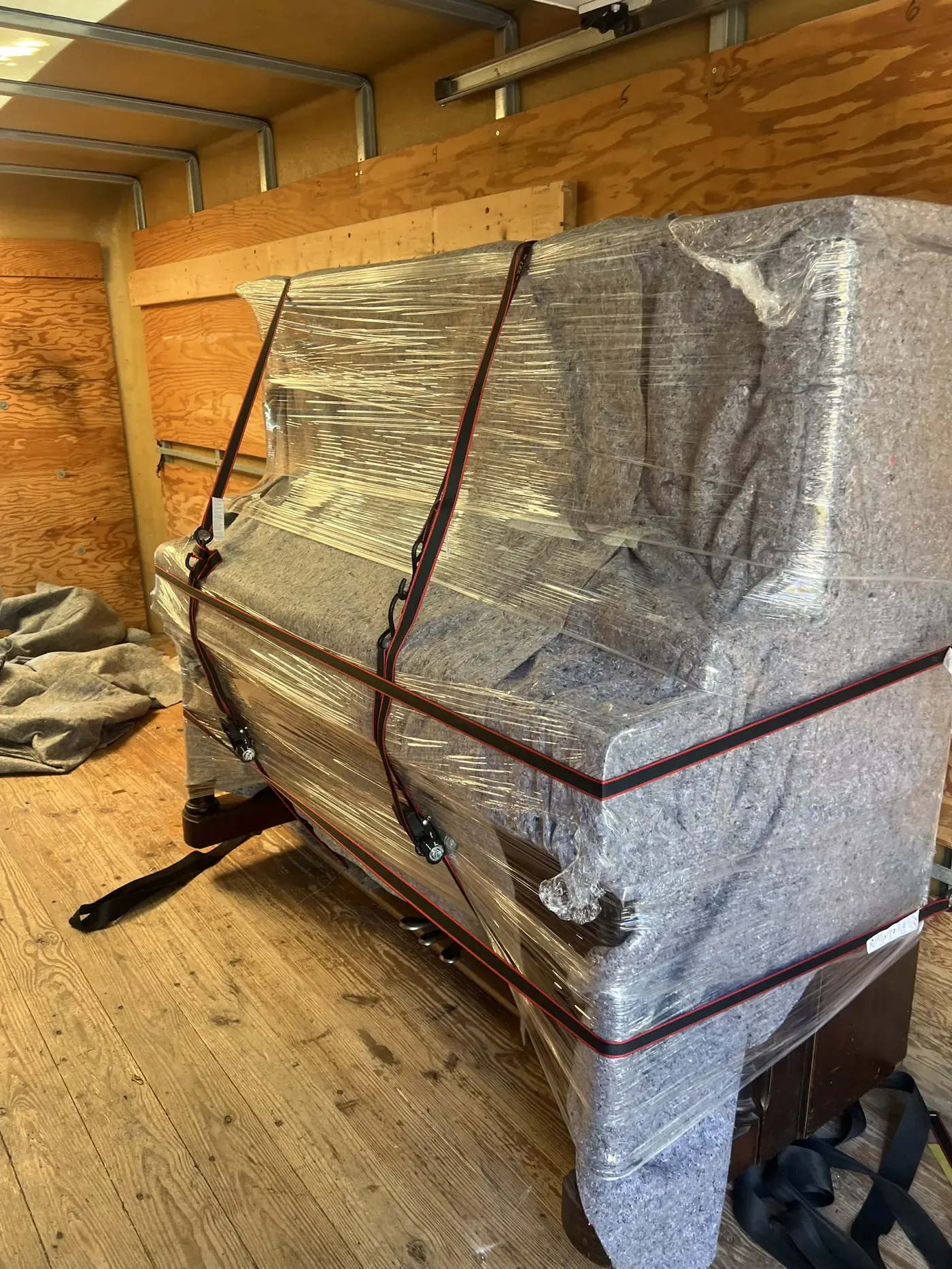 Wrapped piano protected with moving blankets and stretch wrap before moving