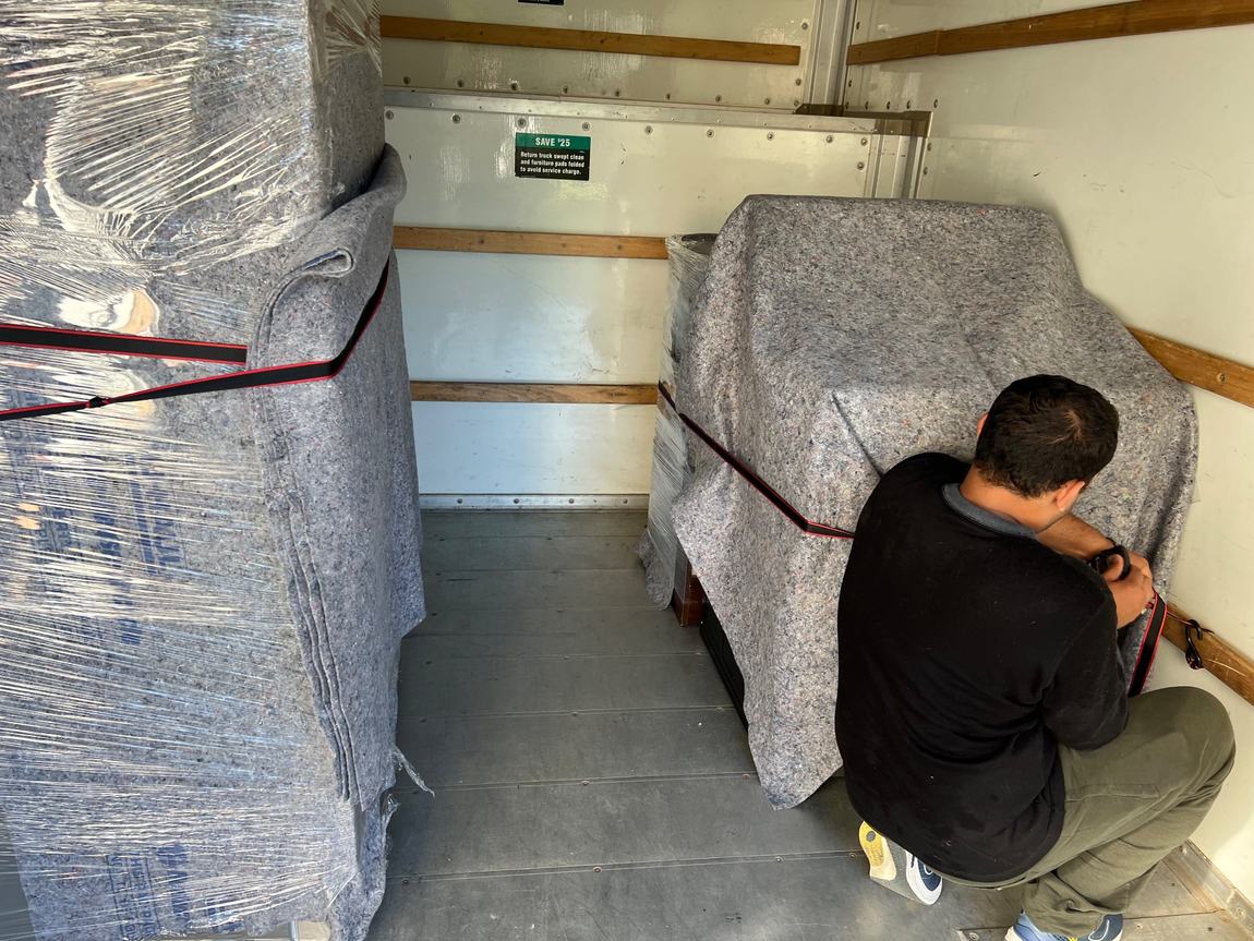 Mover securing furniture wrapped in blankets inside moving truck