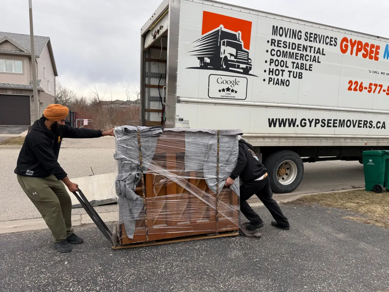 Movers guiding a wrapped piano on a piano dolly